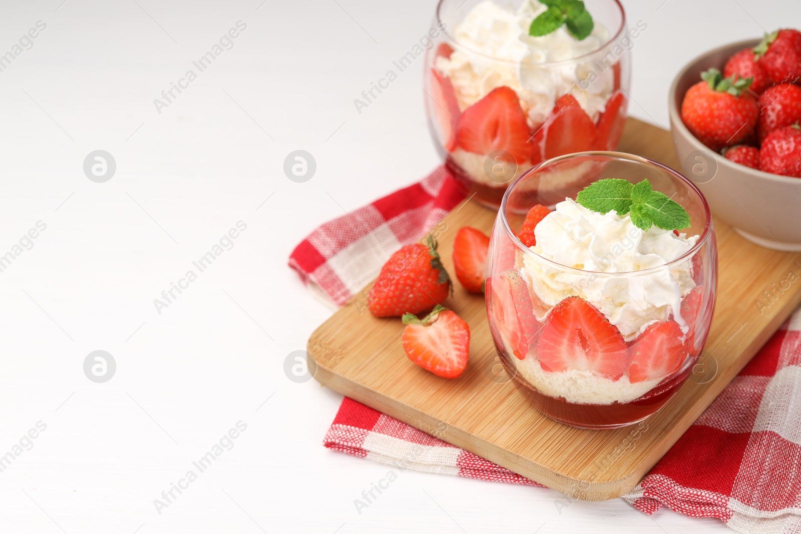 Photo of Tasty trifle dessert. Sponge cake, strawberries, jam and whipped cream in glasses on white table, space for text