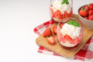 Photo of Tasty trifle dessert. Sponge cake, strawberries, jam and whipped cream in glasses on white table, space for text