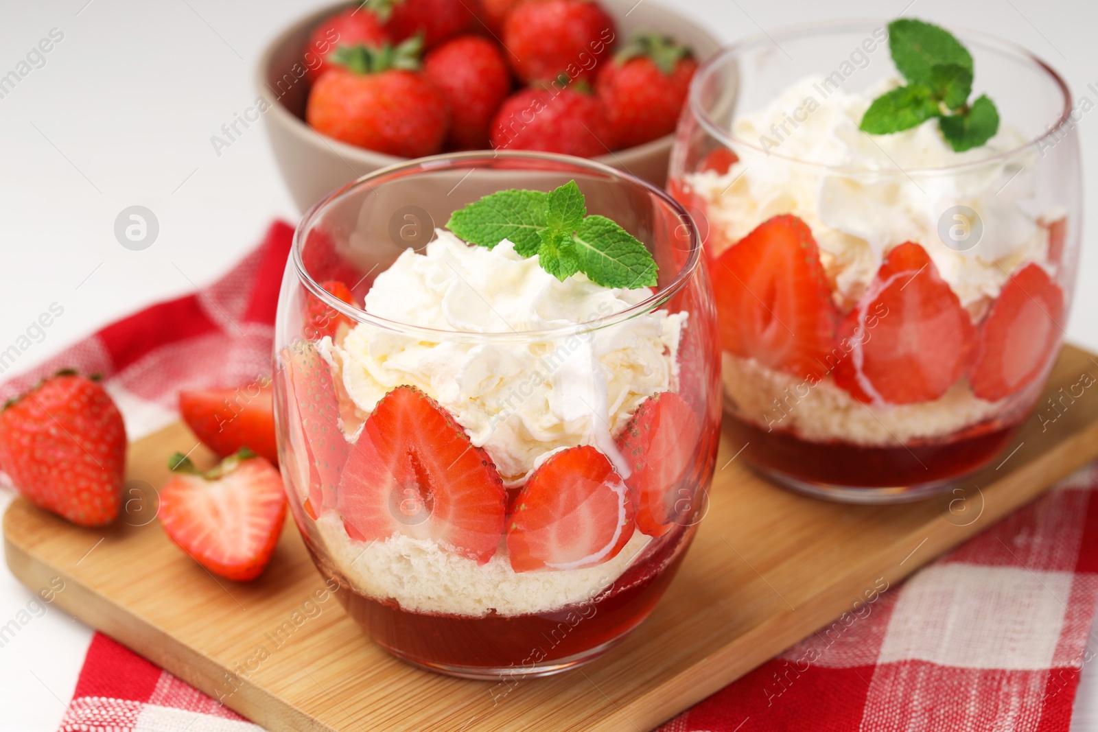 Photo of Tasty trifle dessert. Sponge cake, strawberries, jam and whipped cream in glasses on table, closeup