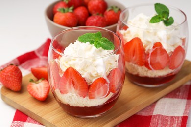 Photo of Tasty trifle dessert. Sponge cake, strawberries, jam and whipped cream in glasses on table, closeup