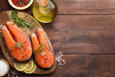 Photo of Fresh raw salmon steaks with spices, lemon, oil and rosemary on wooden table, flat lay. Space for text