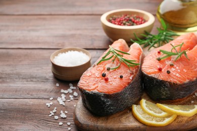 Photo of Fresh raw salmon steaks with spices, lemon and rosemary on wooden table, closeup. Space for text