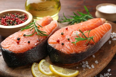 Photo of Fresh raw salmon steaks with spices, lemon and rosemary on wooden table, closeup