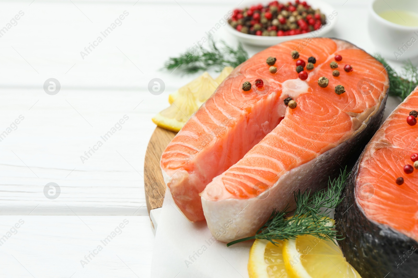 Photo of Fresh raw salmon steaks with peppercorns, lemon and dill on white wooden table, closeup. Space for text