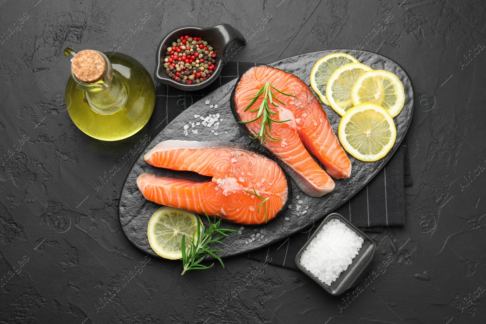 Photo of Fresh raw salmon steaks with salt, lemon, oil, peppercorns and rosemary on dark textured table, flat lay