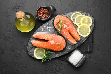 Photo of Fresh raw salmon steaks with salt, lemon, oil, peppercorns and rosemary on dark textured table, flat lay