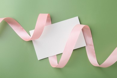 Photo of Blank card and ribbon on green background, top view