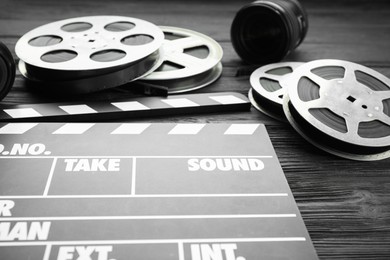 Photo of Movie clapper, camera lens and film reels on black wooden table, closeup