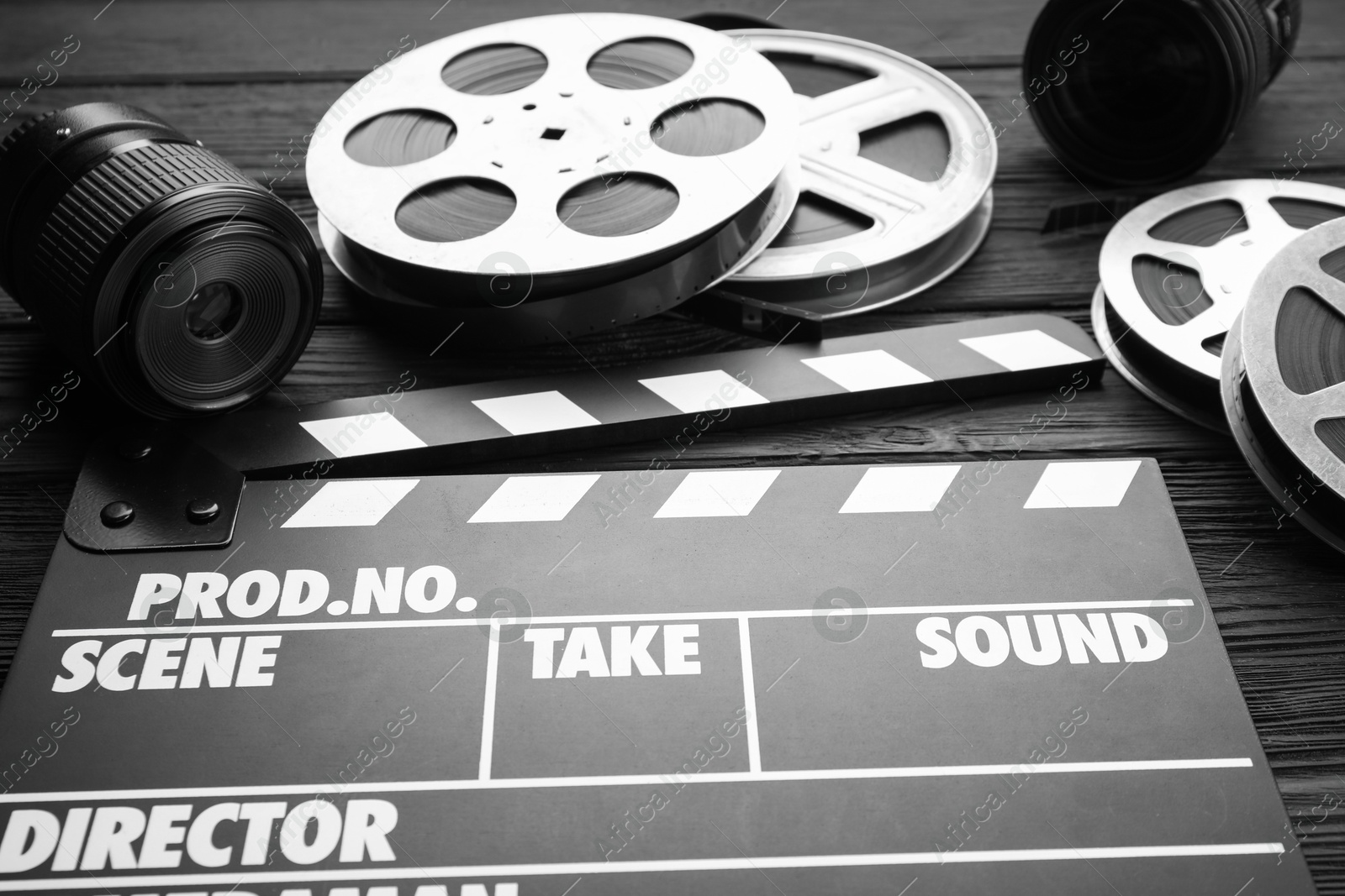 Photo of Movie clapper, camera lens and film reels on black wooden table, closeup