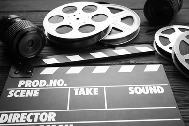 Photo of Movie clapper, camera lens and film reels on black wooden table, closeup