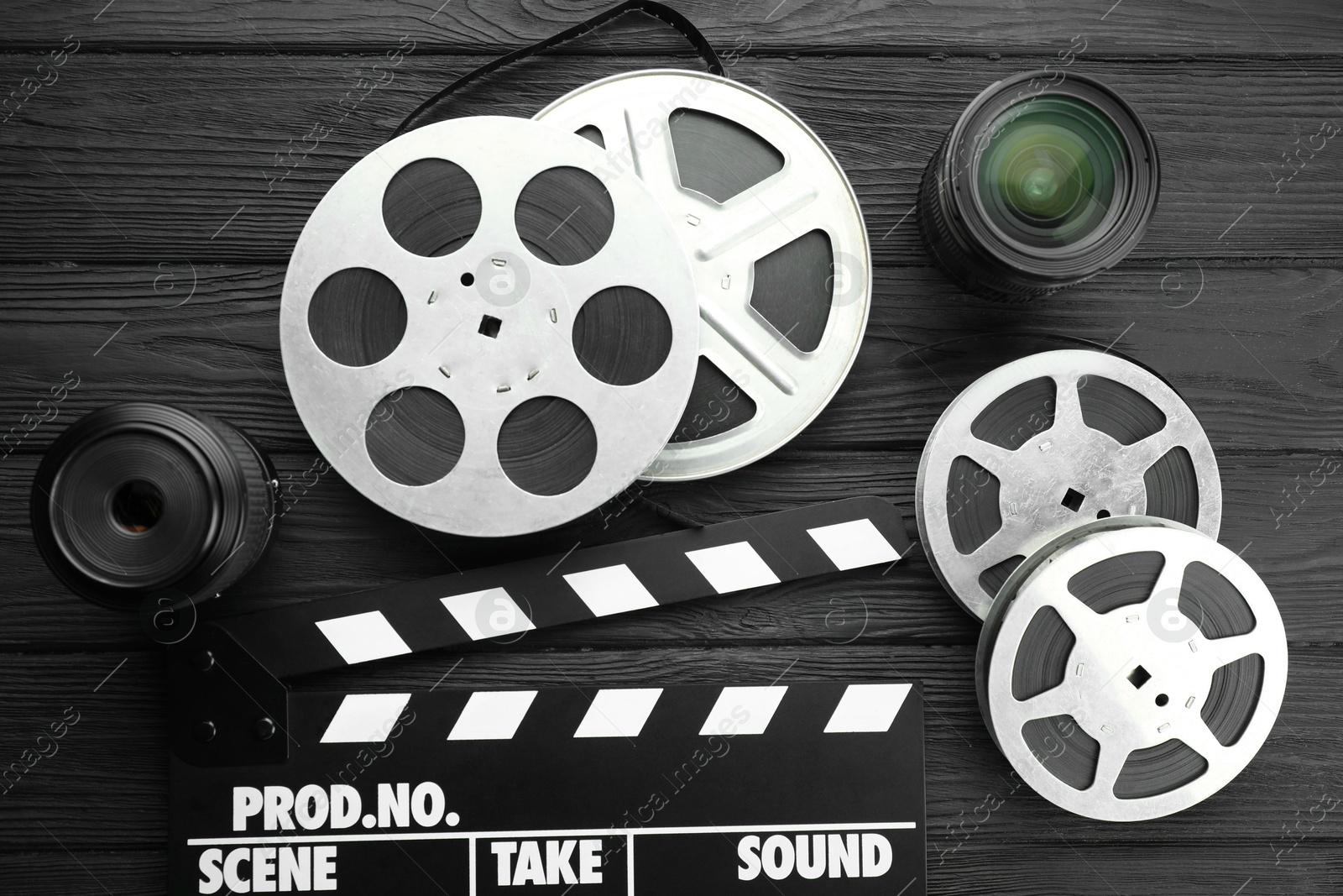 Photo of Movie clapper, camera lens and film reels on black wooden table, flat lay