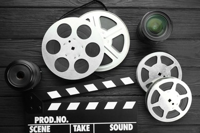 Photo of Movie clapper, camera lens and film reels on black wooden table, flat lay