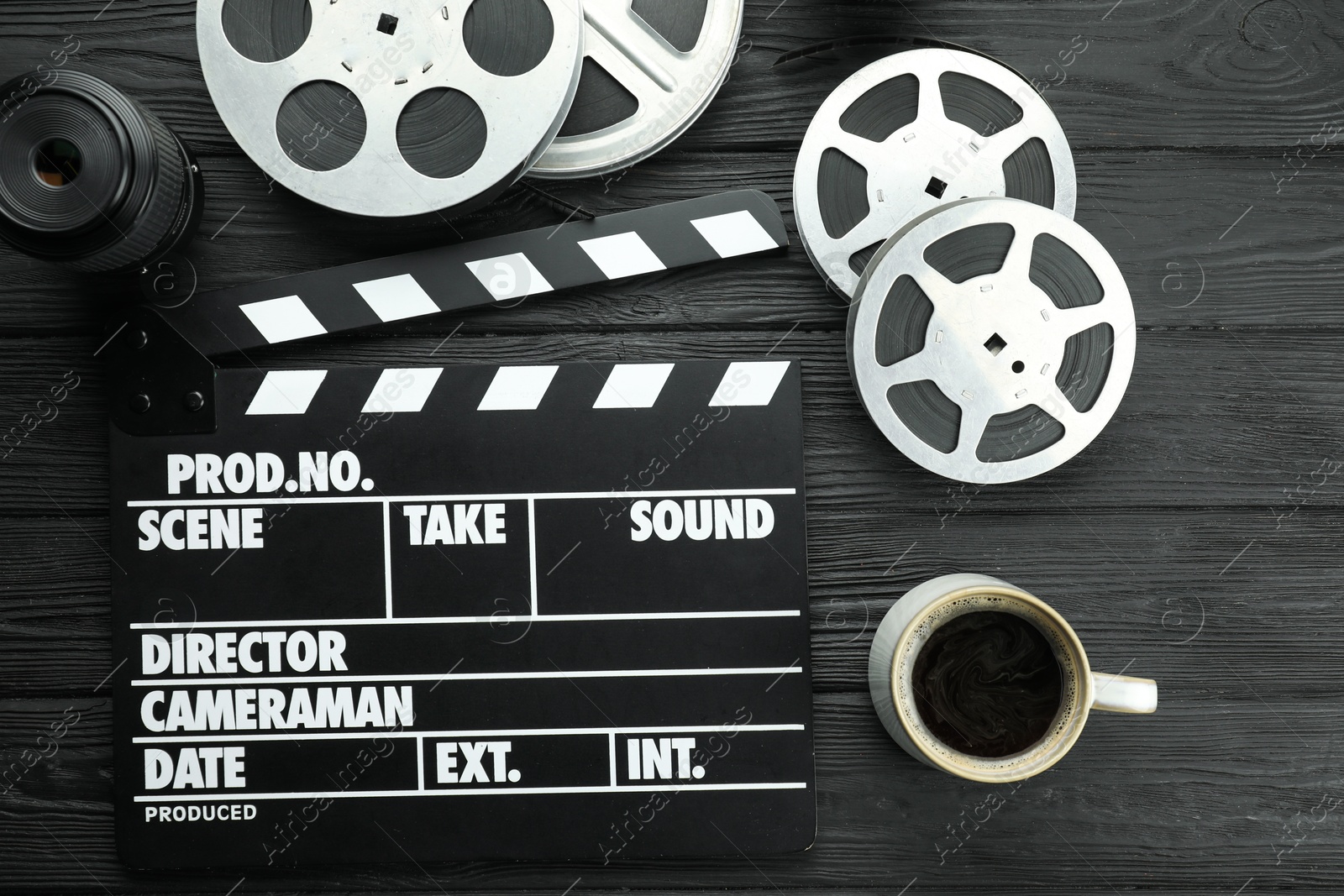 Photo of Movie clapper, camera lens, film reels and cup of coffee on black wooden table, flat lay