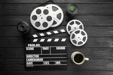 Photo of Movie clapper, camera lens, film reels and cup of coffee on black wooden table, flat lay