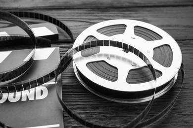 Photo of Movie clapper and film reel on black wooden table, closeup