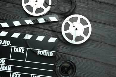 Photo of Movie clapper, film reels and camera lens on black wooden table, flat lay