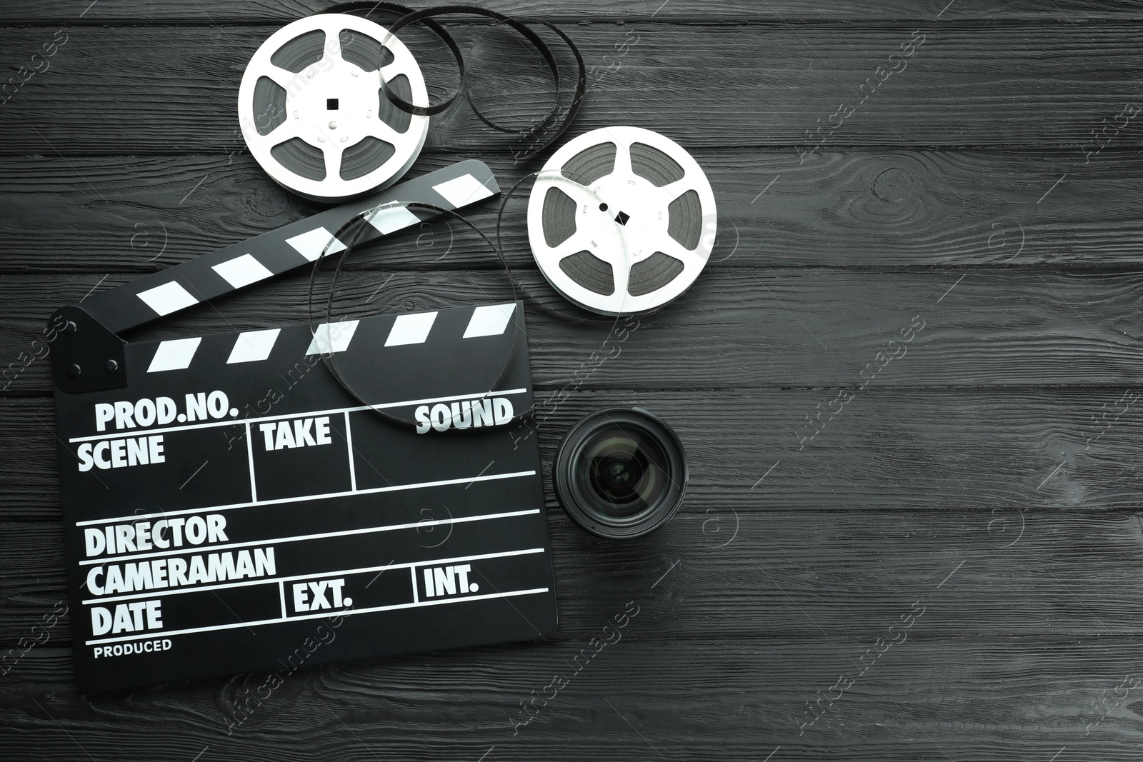 Photo of Movie clapper, film reels and camera lens on black wooden table, flat lay. Space for text