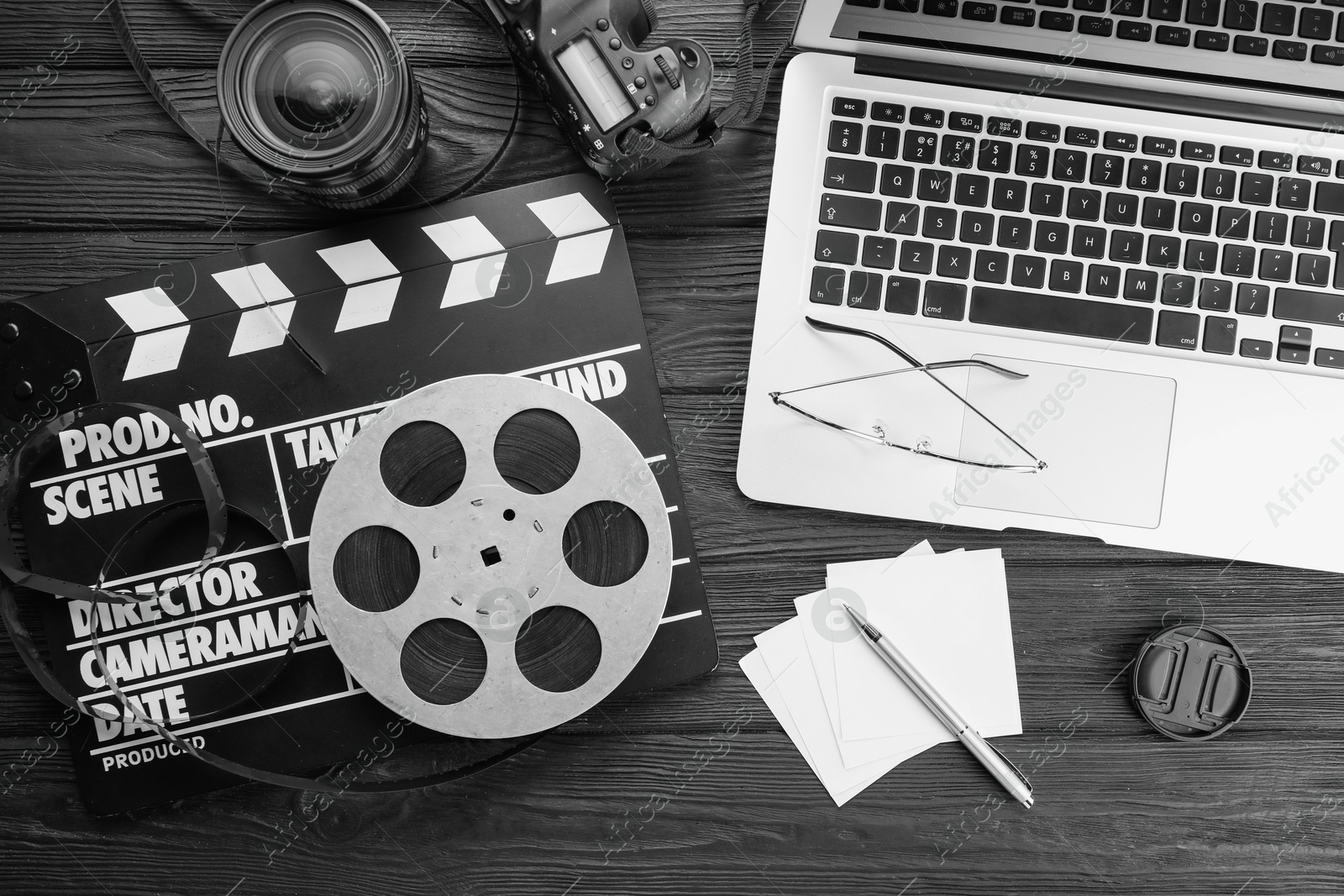 Photo of Movie clapper, film reel, laptop and camera lens on black wooden table, flat lay