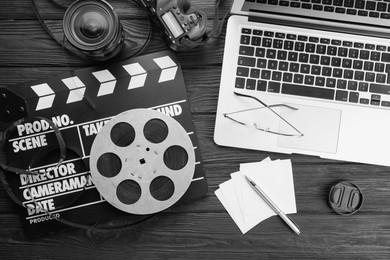 Photo of Movie clapper, film reel, laptop and camera lens on black wooden table, flat lay