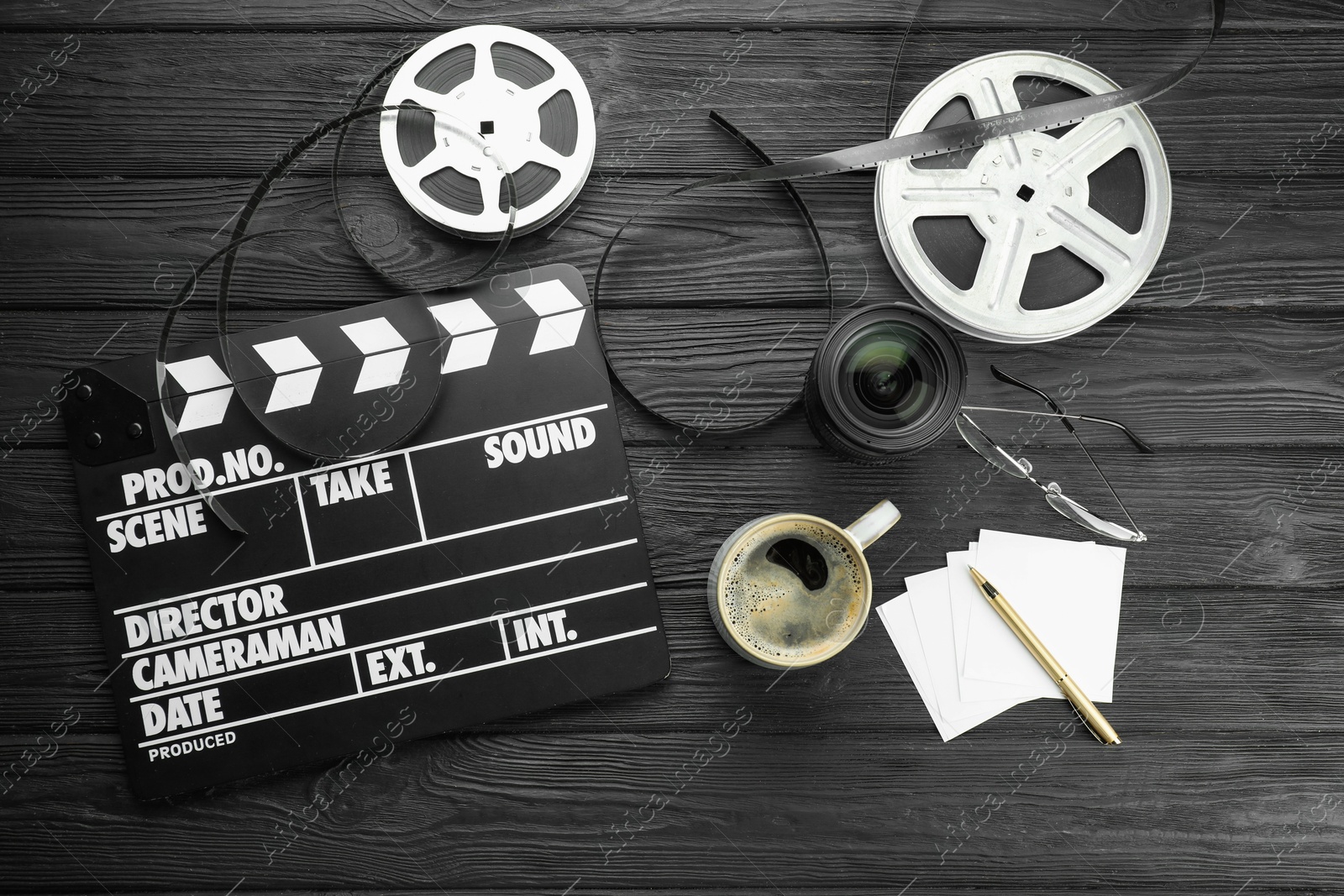 Photo of Movie clapper, film reels and camera lens on black wooden table, flat lay