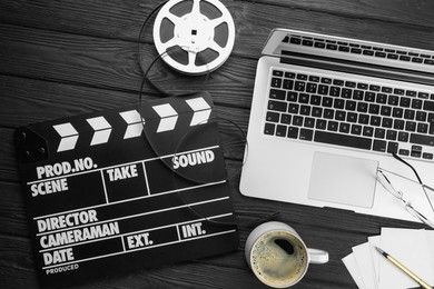 Photo of Movie clapper, film reel, laptop and cup of coffee on black wooden table, flat lay