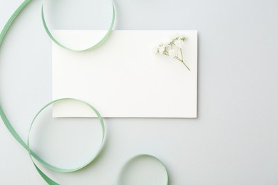 Photo of Blank card, flower and ribbon on light grey table, top view. Space for text