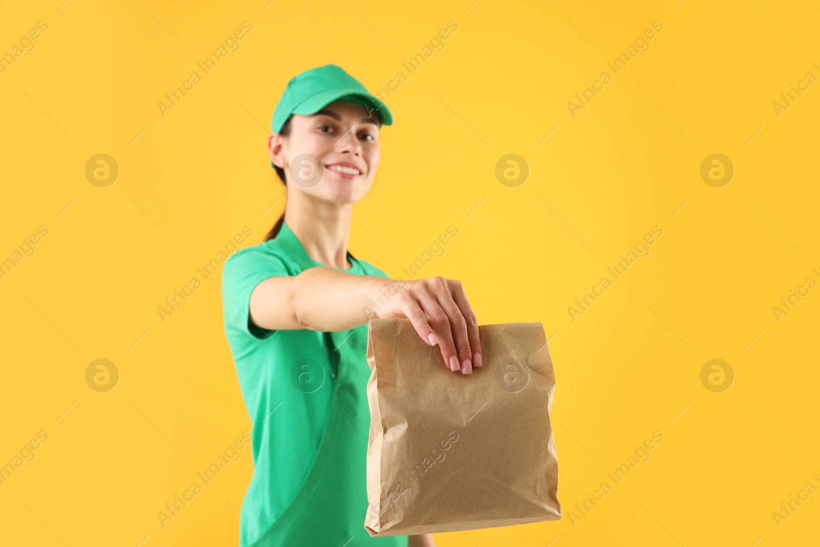 Photo of Fast-food worker with paper bag on orange background, selective focus