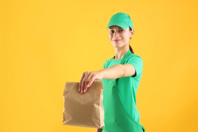 Photo of Fast-food worker with paper bag on orange background, selective focus