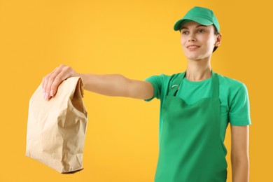 Photo of Fast-food worker with paper bag on orange background, selective focus