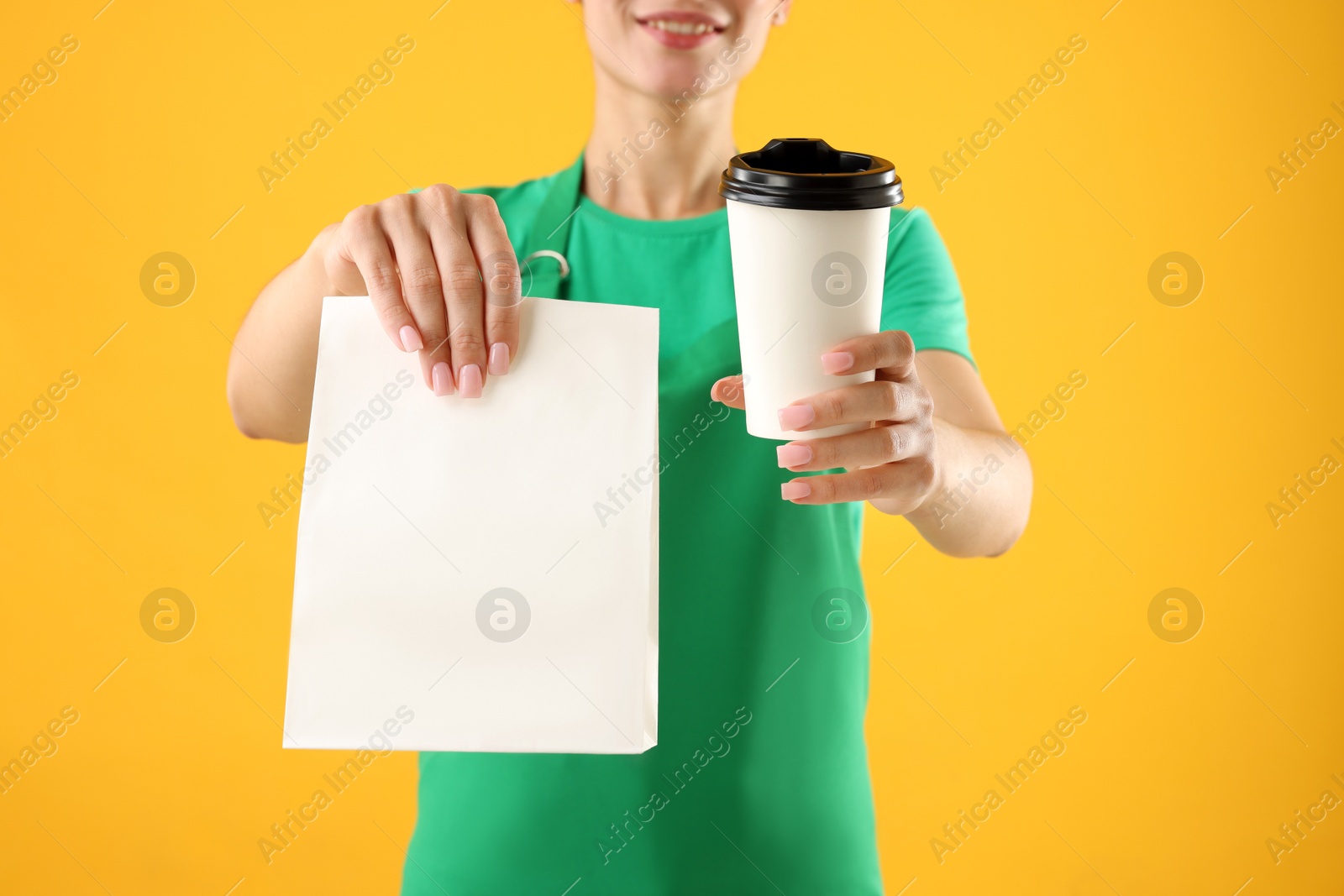 Photo of Fast-food worker with paper bag and cup on orange background, closeup