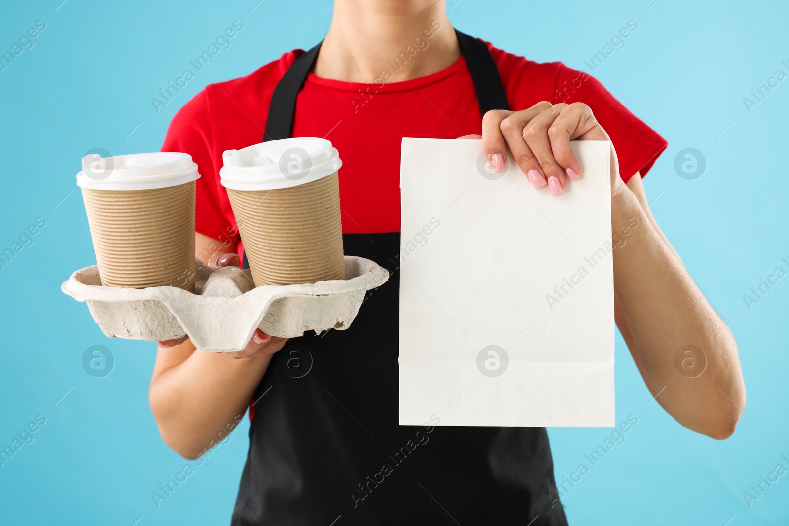 Photo of Fast-food worker with paper cups and bag on light blue background, closeup