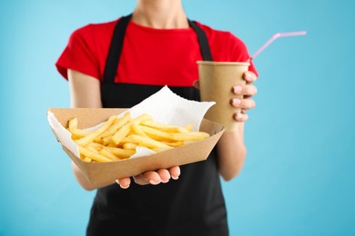 Photo of Fast-food worker with paper cup and fries on light blue background, closeup