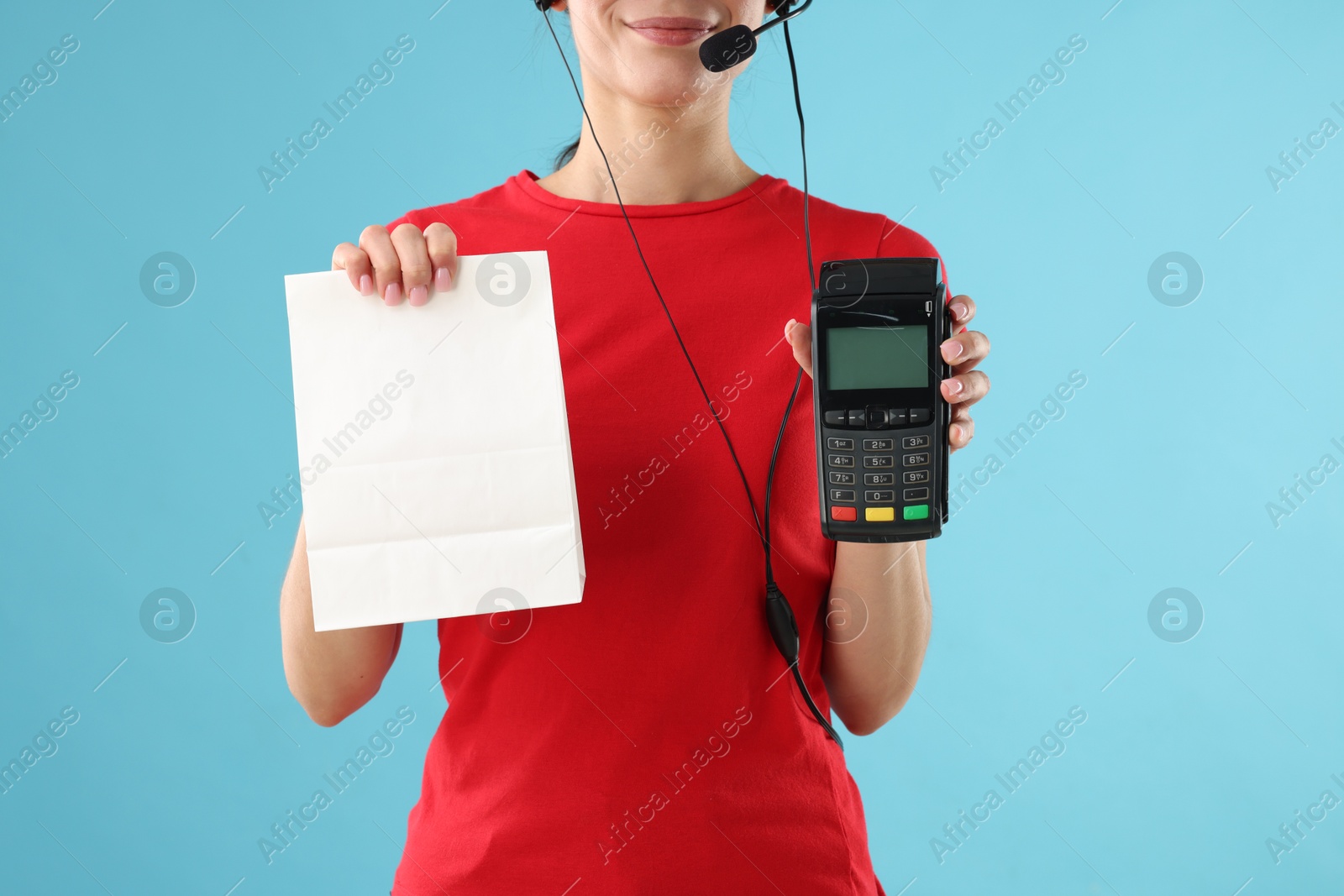 Photo of Fast-food worker with paper bag and payment terminal on light blue background, closeup