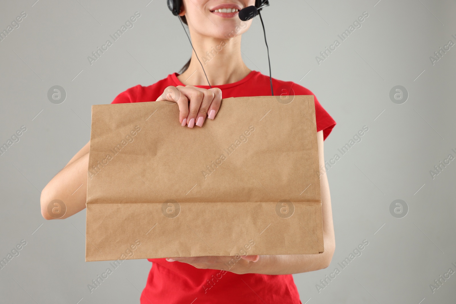 Photo of Fast-food worker with paper bag on gray background, closeup