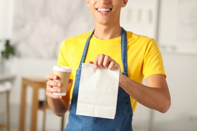 Photo of Fast-food worker with paper bag and cup indoors, closeup