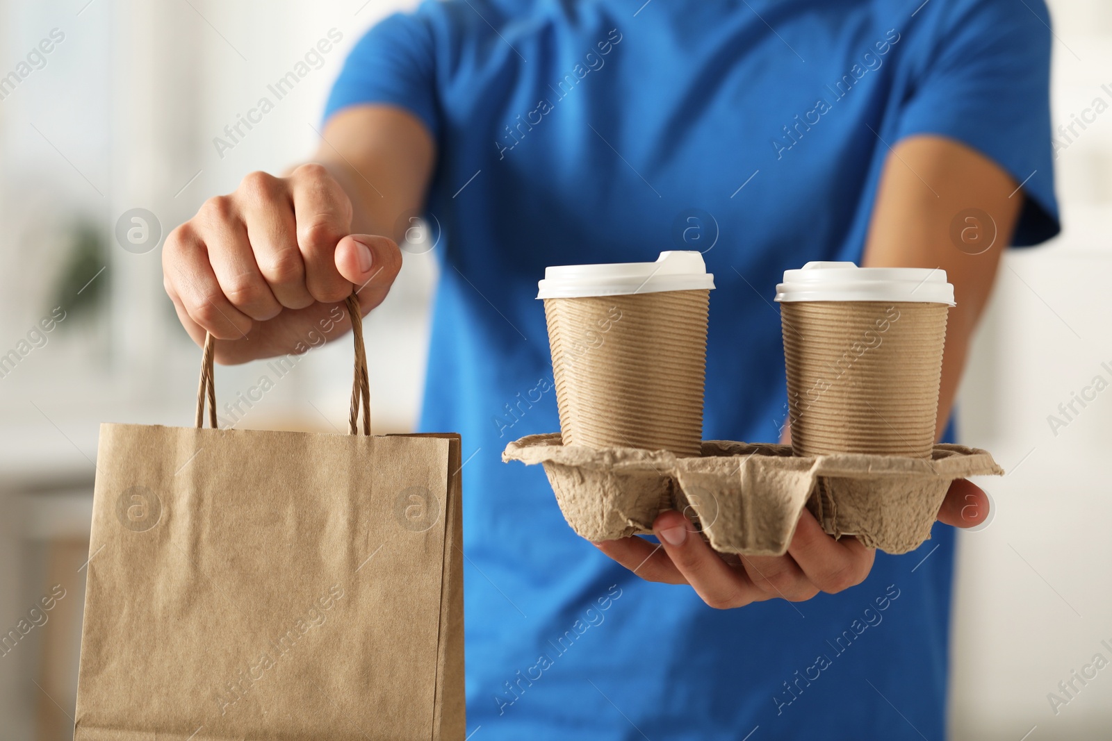 Photo of Fast-food worker with paper bag and cups indoors, closeup