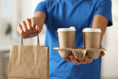 Fast-food worker with paper bag and cups indoors, closeup