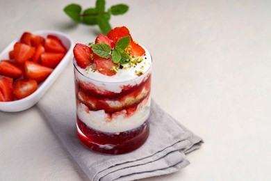 Photo of Tasty trifle dessert. Strawberries, sponge cake and whipped cream in glass on beige table, space for text