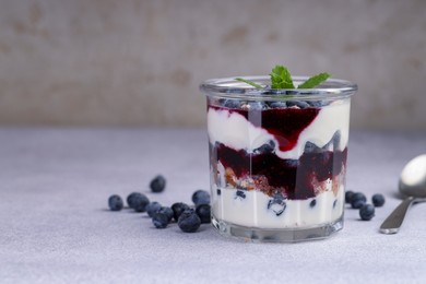 Photo of Tasty trifle dessert. Blueberries, sponge cake and whipped cream in glass on light grey table