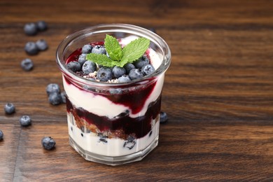 Photo of Tasty trifle dessert. Blueberries, sponge cake and whipped cream in glass on wooden table