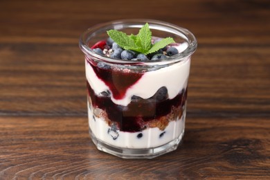 Photo of Tasty trifle dessert. Blueberries, sponge cake and whipped cream in glass on wooden table