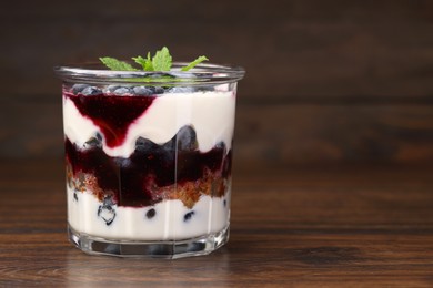 Photo of Tasty trifle dessert. Blueberries, sponge cake and whipped cream in glass on wooden table, space for text