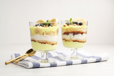 Photo of Tasty trifle dessert. Banana, blueberries, sponge cake and whipped cream in glasses on white wooden table