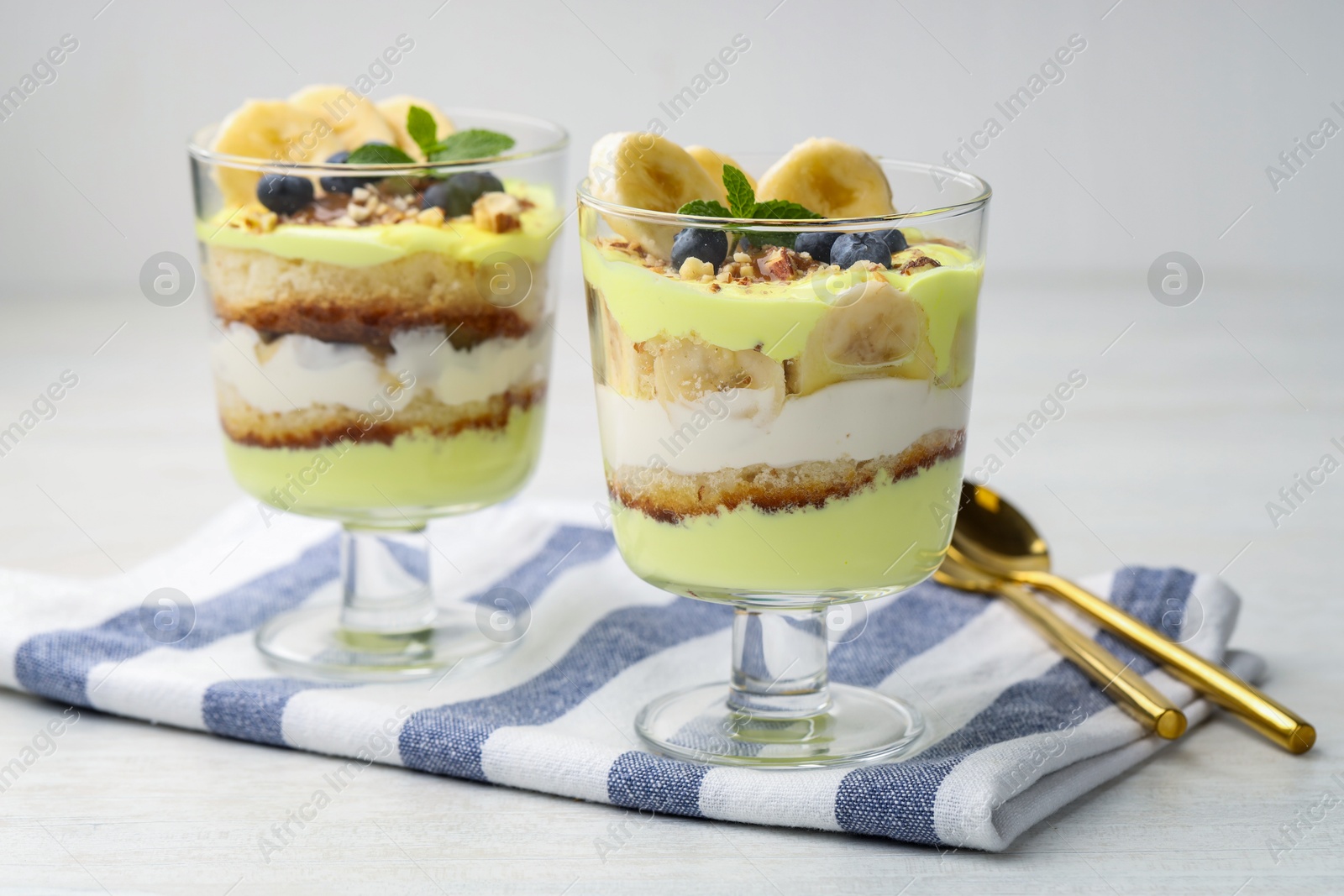 Photo of Tasty trifle dessert. Banana, blueberries, sponge cake and whipped cream in glasses on white wooden table