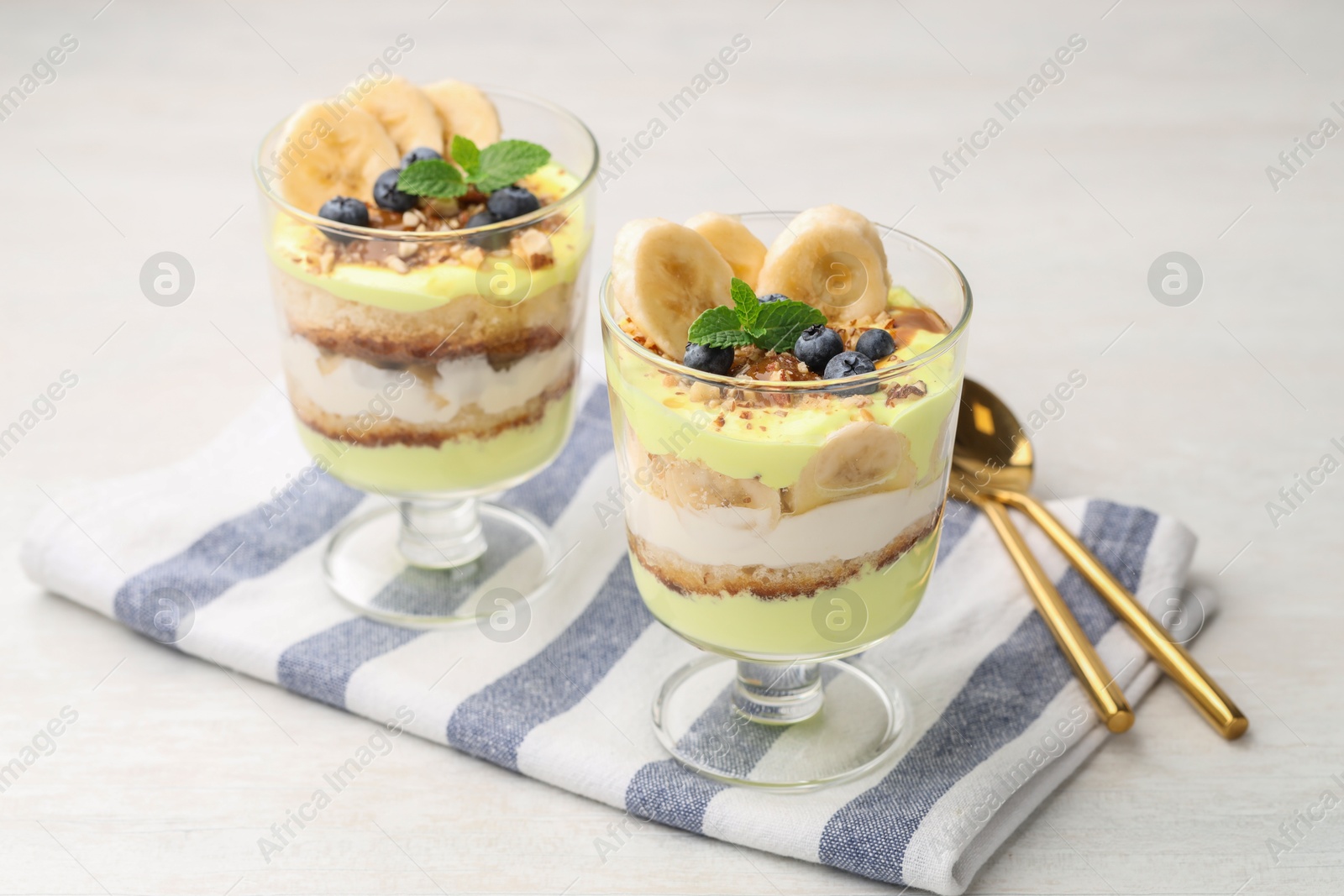 Photo of Tasty trifle dessert. Banana, blueberries, sponge cake and whipped cream in glasses on white wooden table