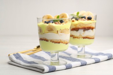 Photo of Tasty trifle dessert. Banana, blueberries, sponge cake and whipped cream in glasses on white wooden table