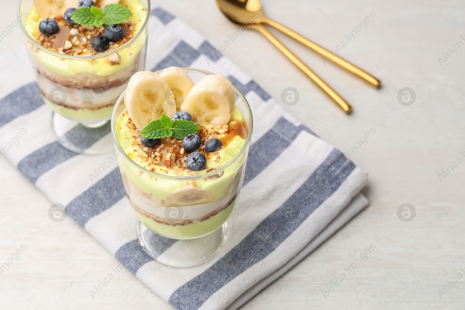 Photo of Tasty trifle dessert. Banana, blueberries, sponge cake and whipped cream in glasses on white wooden table