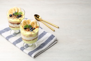 Photo of Tasty trifle dessert. Banana, blueberries, sponge cake and whipped cream in glasses on white wooden table, space for text