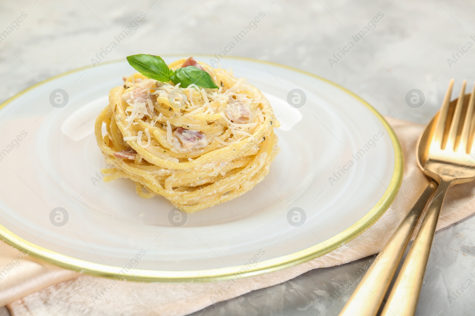 Photo of Plate with delicious pasta Carbonara and cutlery on grey textured table, closeup