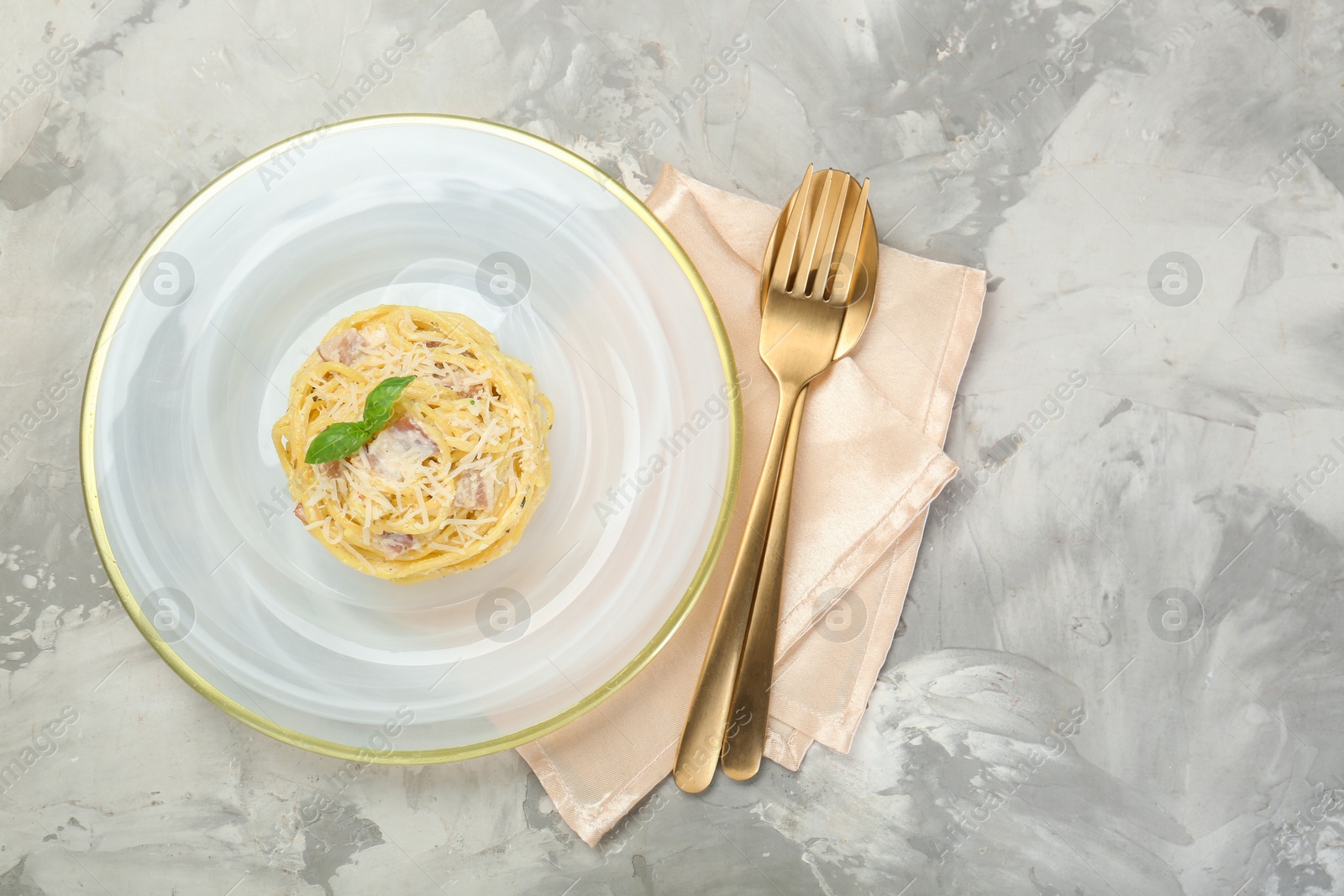 Photo of Plate with delicious pasta Carbonara and cutlery on grey textured table, top view